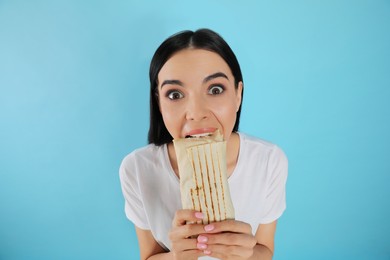 Photo of Emotional young woman eating delicious shawarma on light blue background