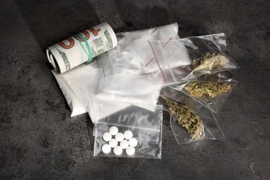 Plastic bags with cocaine, pills, hemp buds and money on grey background