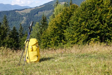Yellow backpack and trekking poles outdoors on sunny day. Mountain tourism