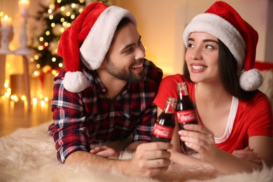 MYKOLAIV, UKRAINE - JANUARY 27, 2021: Young couple holding bottles of Coca-Cola at home. Christmas atmosphere