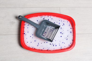 Cat tray with crystal litter and scoop on wooden floor, top view