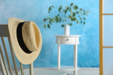 Stylish straw hat hanging on chair in room, space for text