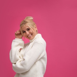 Happy woman in stylish sweater on pink background. Space for text