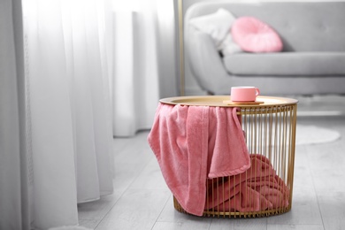 Side basket table with cup of coffee and blanket in modern room interior