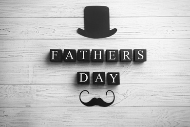 Paper hat, moustache and cubes on wooden background, top view. Father's day celebration