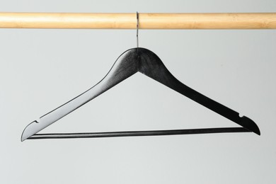 Black clothes hanger on wooden rail against light grey background
