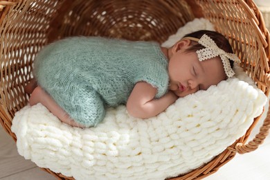 Adorable newborn baby sleeping in wicker basket with soft plaid