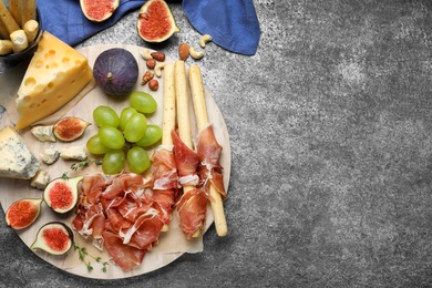Photo of Board with delicious figs, cheese, grapes and bread with proscuitto on grey table, flat lay. Space for text