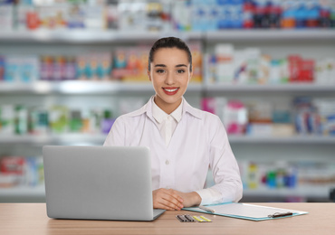 Professional pharmacist working at table in modern drugstore 