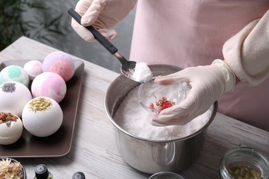 Woman in gloves making bath bomb at wooden table indoors, closeup