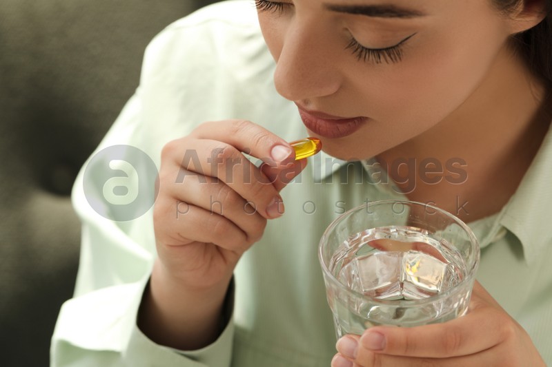 Young woman with glass of water taking dietary supplement pill, closeup