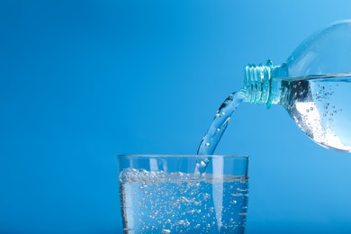 Pouring soda water from bottle into glass on light blue background, closeup. Space for text