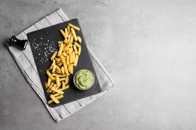 Serving board with french fries and avocado dip on grey table, top view. Space for text