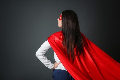 Confident businesswoman wearing superhero cape and mask on grey background, back view
