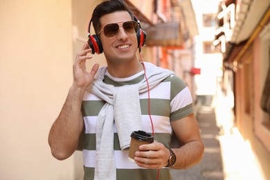 Photo of Happy man with coffee and headphones listening to music on city street