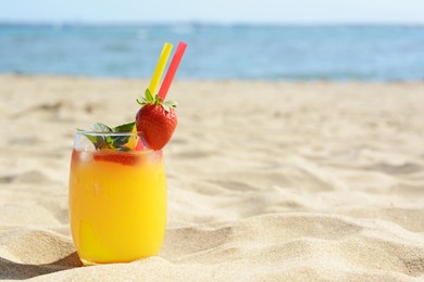 Glass of refreshing drink with strawberry on sandy beach near sea, space for text