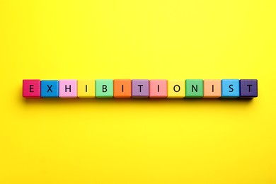 Photo of Word EXHIBITIONIST made with colorful cubes on yellow background, flat lay