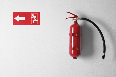 Fire extinguisher and emergency exit sign on white wall