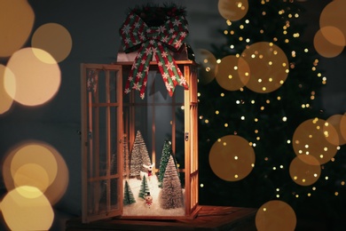 Vintage wooden lantern with beautiful Christmas composition surrounded by blurred festive lights indoors