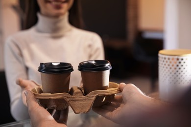 Barista giving takeaway coffee cups to client in cafe, closeup