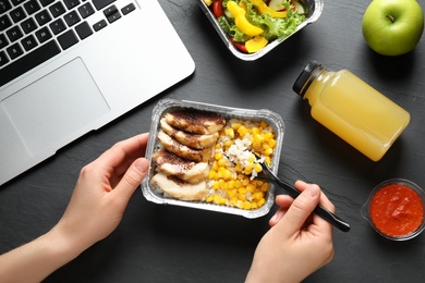 Woman eating from lunchbox at grey table, closeup. Healthy food delivery