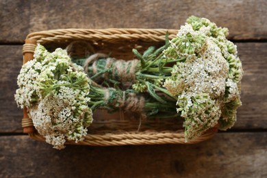 Basket with bunches of beautiful dries yarrow on wooden table, top view