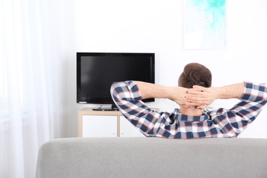 Photo of Young man watching TV on sofa at home