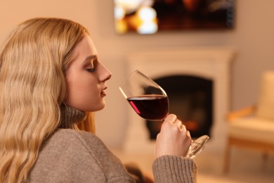 Photo of Beautiful young woman with glass of wine resting near fireplace at home
