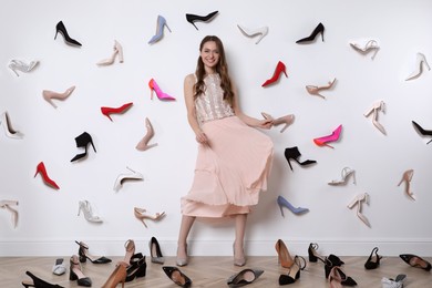 Fashionable young woman surrounded by many different high heel shoes indoors