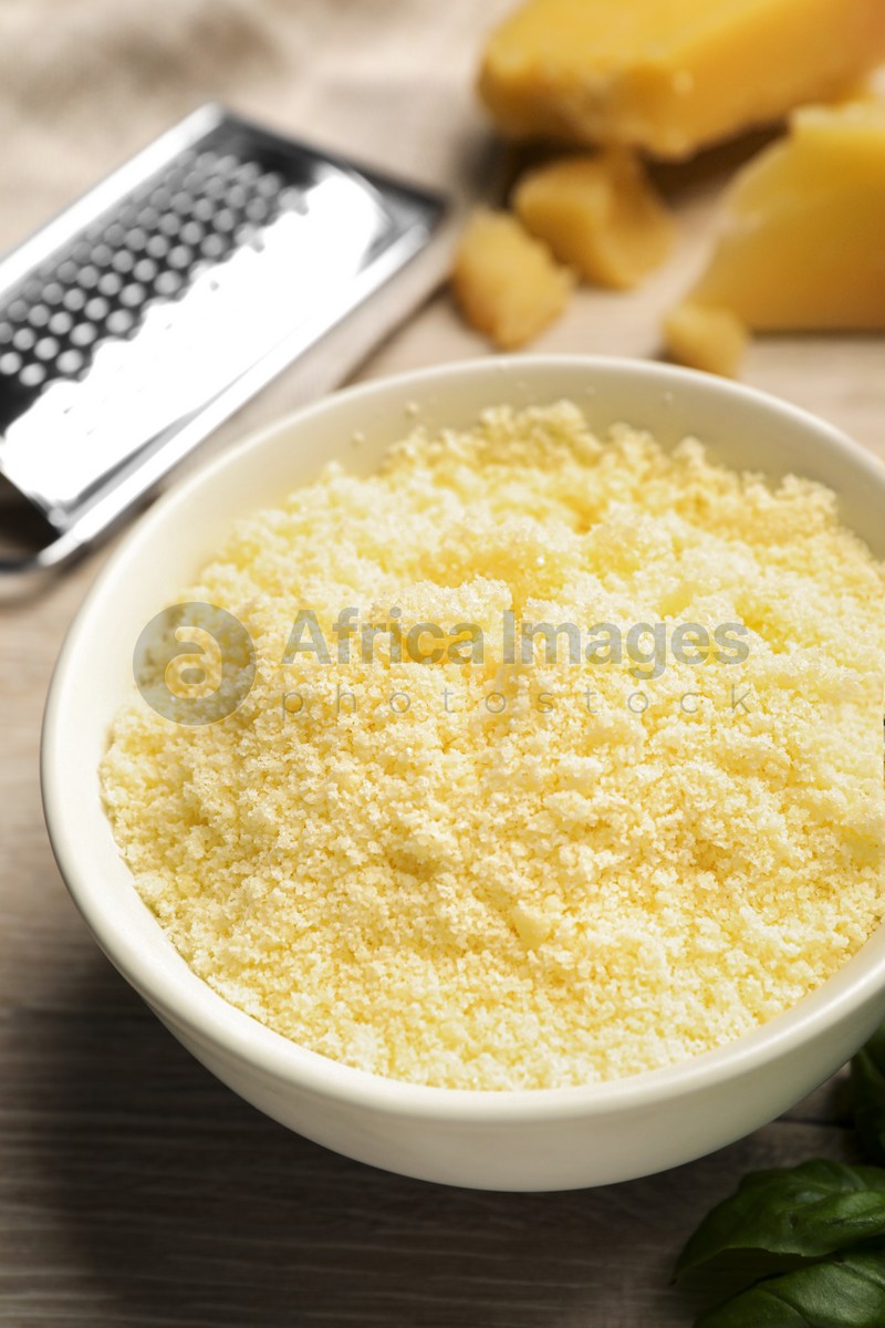 Delicious grated parmesan cheese in bowl on white wooden table, closeup