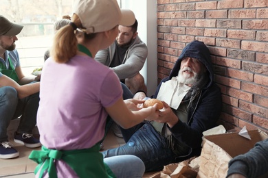 Volunteer giving food to poor senior man indoors