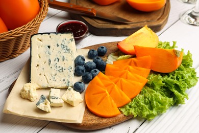 Photo of Delicious persimmon, blue cheese and blueberries served on white wooden table