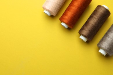 Different colorful sewing threads on yellow background, flat lay. Space for text