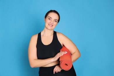 Happy overweight woman with yoga mat on light blue background