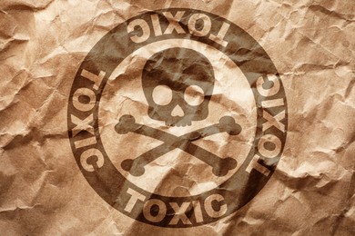 Image of Hazard warning sign (skull-and-crossbones symbol and word TOXIC) on crumpled kraft paper, top view