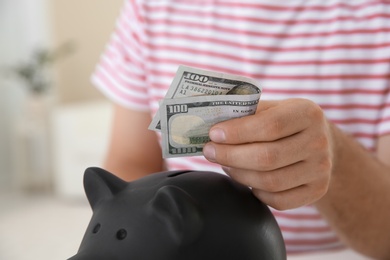 Man putting money into piggy bank on blurred background, closeup