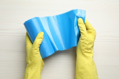 Photo of Janitor in rubber gloves holding roll of light blue garbage bags over white wooden table, top view
