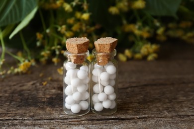 Bottles with homeopathic remedy on wooden table near flowers, closeup