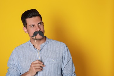 Photo of Man with fake mustache on yellow background. Space for text