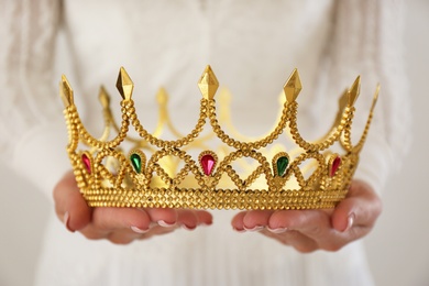 Woman holding beautiful crown with gems on light background, closeup. Fantasy medieval period