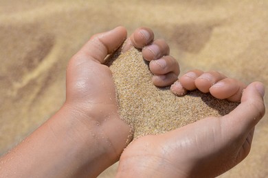Child holding sand in hands outdoors, closeup. Fleeting time concept