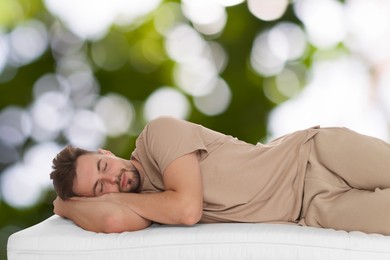 Man sleeping on comfortable mattress against blurred green background, bokeh effect. Sleep well - stay healthy