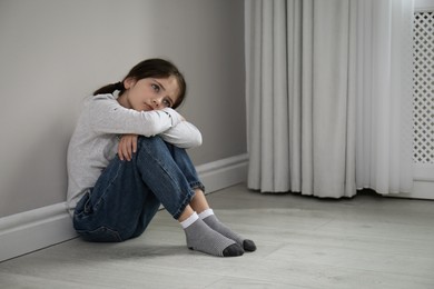 Sad little girl sitting on floor indoors, space for text