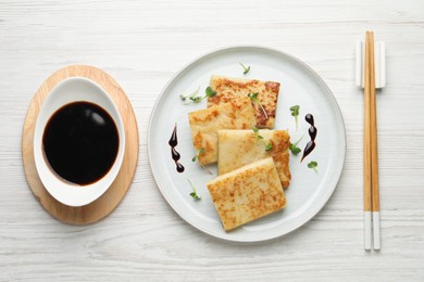 Delicious turnip cake and soy sauce served on white wooden table, flat lay