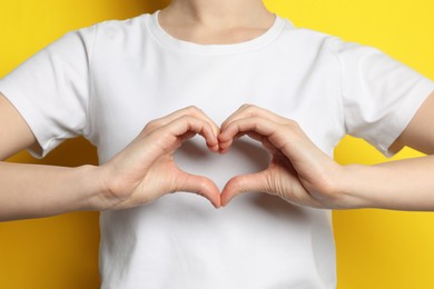 Woman making heart with hands on yellow background, closeup