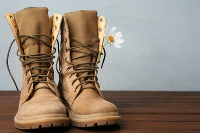 Military boots with flower on wooden surface, space for text. Armed Forces Day