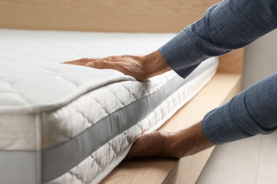 Photo of Man touching soft white mattress indoors, closeup