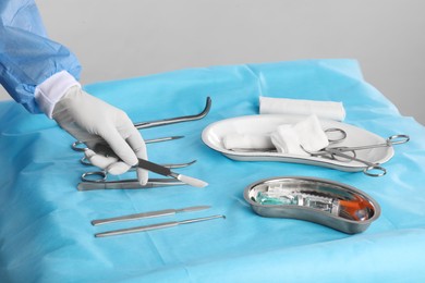 Doctor holding scalpel over table with surgical instruments against light background, closeup
