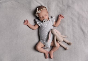 Adorable newborn baby with pacifier and toy bunny sleeping on bed, top view