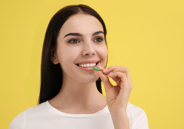 Young woman taking vitamin capsule on yellow background